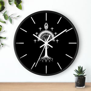 May include: A black wall clock featuring a white tree graphic with roots, a crown, and stars. The clock has white hands and white markers for the hours. The clock is round and has a black frame.
