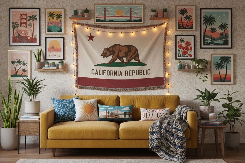 May include: A mustard yellow sofa with four decorative pillows and a blue and white throw blanket. Above the sofa hangs a California Republic flag tapestry with a brown bear, a red star, and string lights. The wall features several framed art prints.