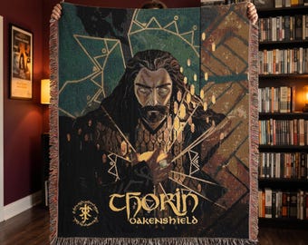 May include: A woven throw blanket featuring a portrait of Thorin Oakenshield with long dark hair and a beard. The design includes gold geometric accents, a circular emblem, and the text Thorin Oakenshield in a stylized font with fringed edges.
