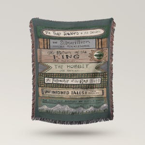 May include: A green throw blanket with a design of stacked book spines. The titles on the spines include "The Two Towers," "The Silmarillion," "The Return of the King," "The Hobbit," "The Fellowship of the Ring," and "Unfinished Tales." It has a fringed edge.