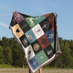 Lord Of The Rings Middle Earth Flags and Symbols woven throw blanket displayed against sky, colorful patchwork design with mythical creatures and magical emblems, decorative fringe trim