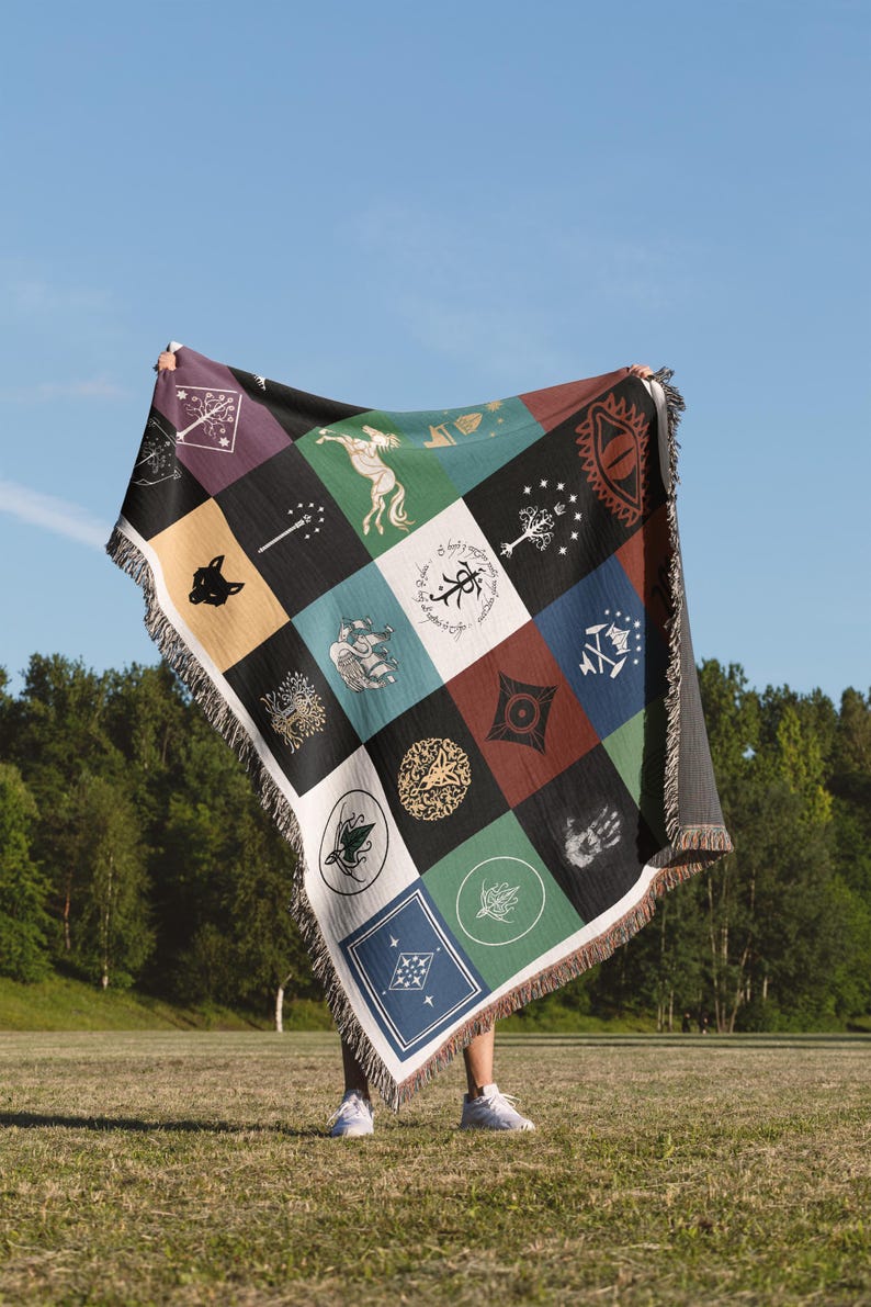 Lord Of The Rings Middle Earth Flags and Symbols woven throw blanket displayed against sky, colorful patchwork design with mythical creatures and magical emblems, decorative fringe trim