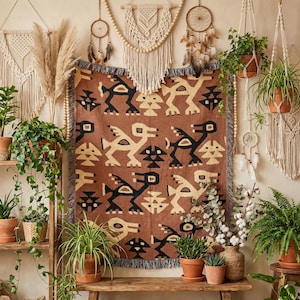 Puede incluir: Una manta tejida rectangular con un patrón repetitivo de aves estilizadas en negro y crema sobre un fondo terracota, terminada con bordes deshilachados. El diseño incluye formas geométricas intercaladas entre las figuras de las aves.