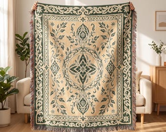 May include: A rectangular woven throw blanket featuring a cream-colored background with a dark green botanical and geometric pattern. The design includes a central medallion, scrolling leaf motifs, and a decorative border with fringed edges.