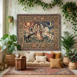 May include: A rectangular tapestry with a celestial design, featuring an angel, horses, sun, and moon. The artwork shows an angel figure between a black and white horse. The tapestry has a fringed border and is displayed above a sofa with decorative cushions.
