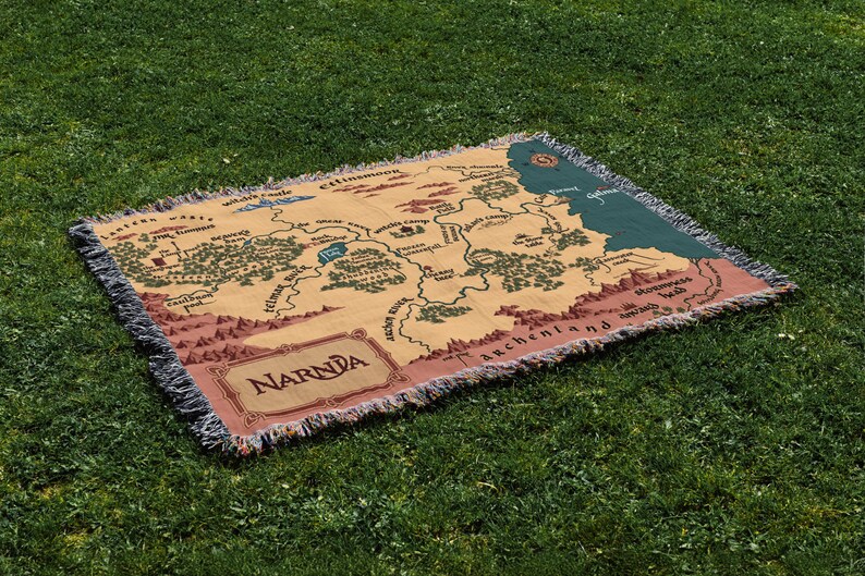 May include: A rectangular woven throw blanket featuring a map of Narnia. The blanket has a tan background with a detailed map design in shades of brown, green, and blue. The word "Narnia" is displayed in a decorative font.