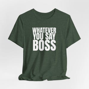 May include: A dark forest green short-sleeved t-shirt featuring the white text "WHATEVER YOU SAY BOSS" printed in a bold, sans-serif font across the centre of the chest. The garment has a classic crew neckline and a heathered fabric texture.