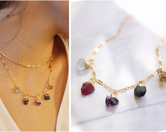 May include: A gold chain necklace with multiple colorful gemstone pendants. The necklace features a variety of stones, including aquamarine, ruby, amethyst, and emerald.