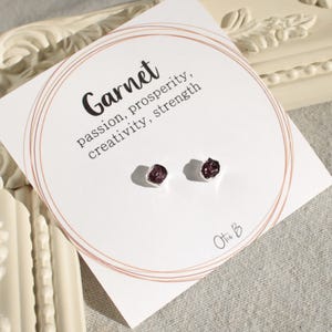 May include: A pair of silver stud earrings with small, raw garnet stones. The card reads "Garnet, passion, prosperity, creativity, strength" and "Otto B."