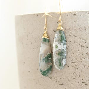 May include: A pair of gold wire wrapped earrings with green and white agate teardrop shaped stones.