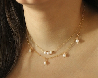 May include: A gold chain necklace with multiple strands and small pearl accents. The necklace features a row of three pearls in the center and dangling pearls on each side.