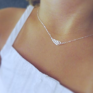 May include: A silver necklace with a delicate wing pendant. The necklace is worn by a person.