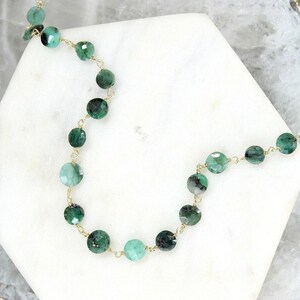 May include: A delicate necklace featuring faceted, round green gemstone beads linked together by thin gold-colored wire. The beads vary in shade from light mint to deep forest green, showcasing natural inclusions and a polished, reflective surface.