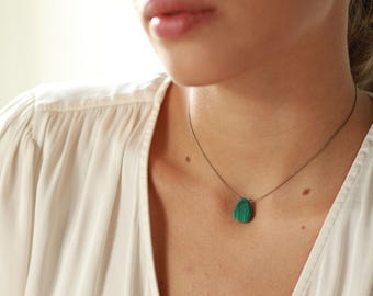 May include: A silver chain necklace with a teardrop-shaped green malachite pendant.