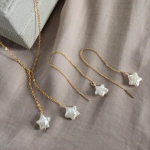 Peut inclure: Un ensemble de collier et de boucles d'oreilles dorées. Le collier a un design en forme de Y avec trois pendentifs en perles blanches en forme d'étoile. Les boucles d'oreilles sont de style fil, avec une perle en forme d'étoile à chaque extrémité.