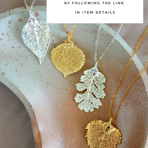 May include: Four leaf pendant necklaces in silver and gold tones. The leaf pendants have intricate, openwork designs. The necklaces are displayed on a neutral-toned surface. Text on the image reads: FIND THE MATCHING NECKLACE BY FOLLOWING THE LINK IN ITEM DETAILS.