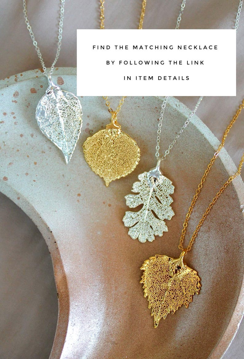 May include: Four leaf pendant necklaces in silver and gold tones. The leaf pendants have intricate, openwork designs. The necklaces are displayed on a neutral-toned surface. Text on the image reads: FIND THE MATCHING NECKLACE BY FOLLOWING THE LINK IN ITEM DETAILS.