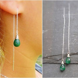 May include: A pair of silver chain earrings with green gemstone drops. The earrings are long and dangle from the earlobe.