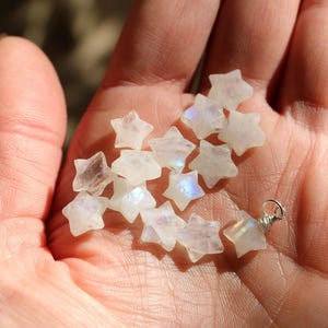 May include: A collection of white moonstone star-shaped beads with iridescent rainbow flashes. The beads are approximately 1/2 inch in size and are perfect for jewelry making.
