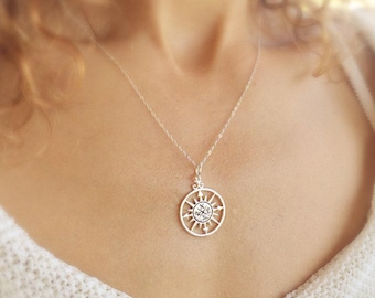 May include: A silver necklace featuring a compass pendant. The compass has a circular design with the letters N, S, E, and W inscribed on it.