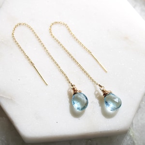 May include: A pair of gold chain earrings with light blue teardrop-shaped gemstones.