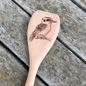 May include: A wooden spoon with a brown and white kookaburra bird design burned into the front of the spoon.