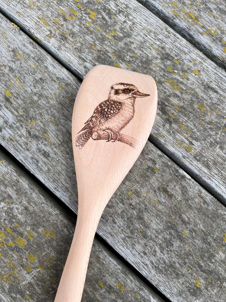 May include: A wooden spoon with a brown and white kookaburra bird design burned into the front of the spoon.