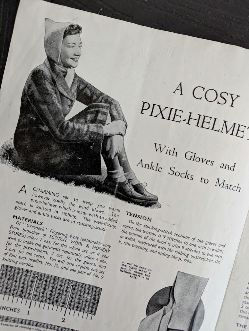 May include: A vintage knitting pattern page titled A COSY PIXIE-HELMET With Gloves and Ankle Socks to Match. It features a black and white illustration of a person wearing the set, along with printed instructions, material lists, and a ruler.