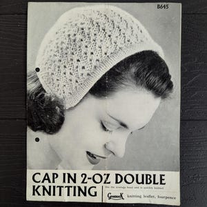 May include: A vintage black and white knitting pattern leaflet titled CAP IN 2-OZ DOUBLE KNITTING with code B645. The leaflet features a photograph of a person wearing a textured, light-coloured knitted cap with a ribbed brim and a Greenock logo.