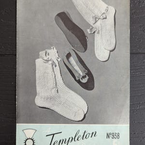 May include: A vintage knitting pattern booklet titled A Templeton Design No 938 featuring illustrations of white knitted socks with ribbon bows and dark slippers with decorative trim on a gray background with a light blue bottom border.