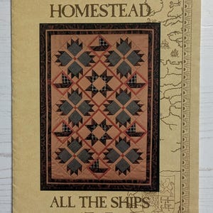 Puede incluir: Un papel de color beige con el texto "LIBERTY HOMESTEAD" y "ALL THE SHIPS AT SEA". El centro presenta un patrón de edredón con cuadrados marrones, negros y beige. El borde tiene un mapa y elementos decorativos.