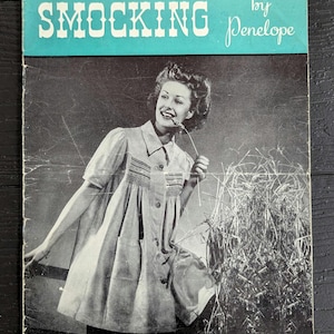 Op de afbeelding: Een vintage instructieboekje getiteld SMOCKING by Penelope uit de serie The Book of Hows. De omslag bevat een zwart-witfoto van een persoon in een gesmokte jurk, staand bij hoog gras, tegen een blauwgroene achtergrond.