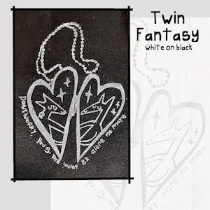 May include: A black and white pendant necklace featuring a heart-shaped design with two stylized animal figures. The pendant has the text "Twin Fantasy" and "white on black". The necklace also has the text "Don't worry, you'll be alone no more."