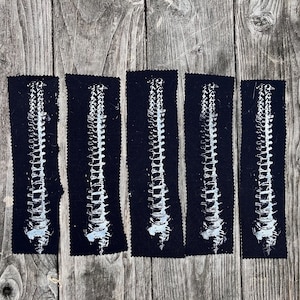 May include: Five rectangular patches with a black background and a white spine design. The spine illustration is centered on each patch. The patches are arranged in a row on a weathered wooden surface.