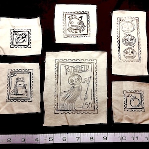 May include: A collection of fabric squares with black ink stamp designs. The stamps feature various whimsical illustrations, including a frog, a face with the text "IT'S A ROCK FACE", and a figure with the text "POTTERFIELD". Measurements are shown in inches.