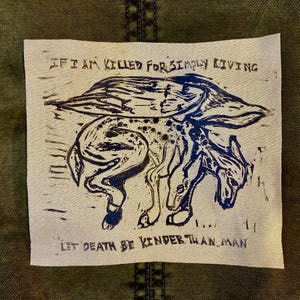 May include: A square, off-white patch with a dark blue linocut print of a mythical creature. The text at the top reads "IF I AM KILLED FOR SIMPLY LIVING" and the text at the bottom reads "LET DEATH BE KINDER THAN MAN."