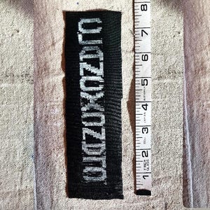 May include: A black rectangular patch with the word "ZUKUZDTO" in white block letters. The patch is approximately 3 inches long. A measuring tape is next to the patch, showing the length.