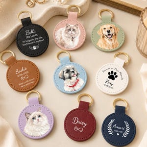 Puede incluir: Una colección de nueve llaveros circulares de cuero con retratos de mascotas personalizados o textos conmemorativos. Los llaveros vienen en varios colores, incluyendo negro, tostado, azul claro, blanco, lavanda, granate y azul marino.