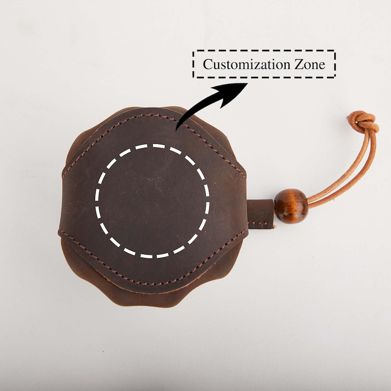 May include: A brown leather item with a circular design, featuring a dotted circle for customization. It has a leather strap with a wooden bead and a knotted end. The text "Customization Zone" is above the item.