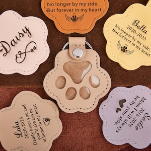 May include: A collection of personalized pet memorial keychains in various colors, including tan, orange, and lavender. Each keychain features a paw print or a scalloped edge with a pet's name, dates, and a heartfelt message. The keychains are made of leather.