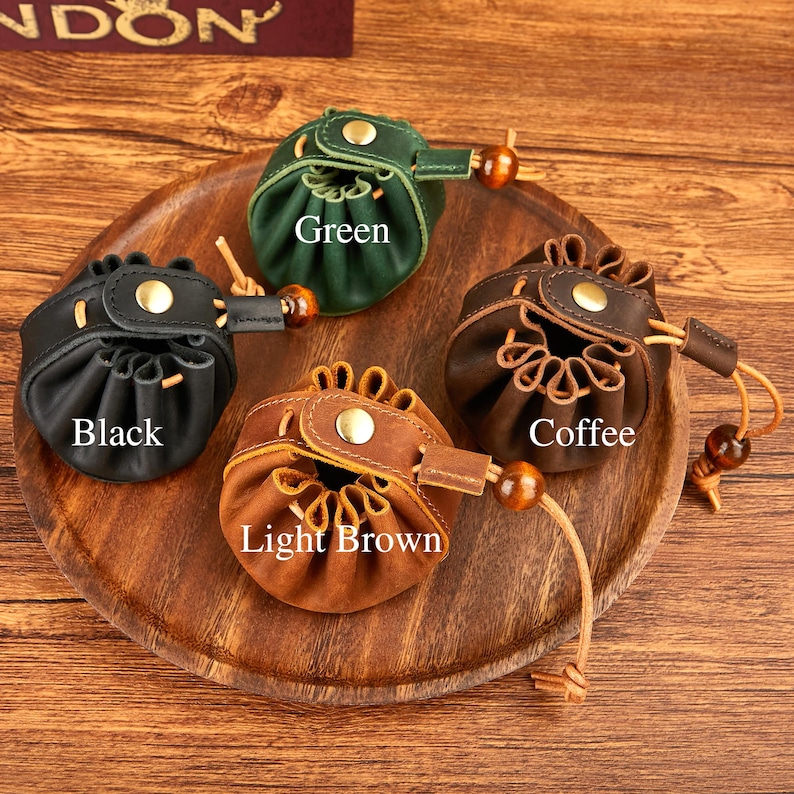 May include: Four small leather pouches in black, green, light brown, and coffee colors, each with a drawstring closure and a wooden bead accent. The pouches are displayed on a wooden tray, with the color names printed on each pouch.