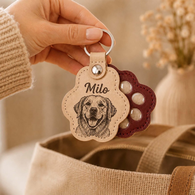 May include: A paw-shaped keychain featuring a light tan front layer with an engraved portrait of a dog and the name Milo, attached to a dark maroon back layer with circular cutouts, all secured by a silver metal ring and a central rivet.