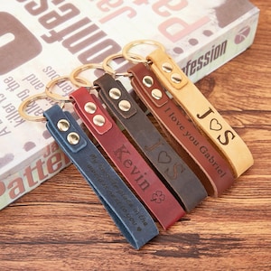 Puede incluir: Varios llaveros de cuero en diferentes colores, incluyendo azul, rojo, marrón y beige. Cada llavero tiene un anillo dorado y está grabado con textos como "Kevin", "I love you Gabriel" y otros mensajes personalizados.