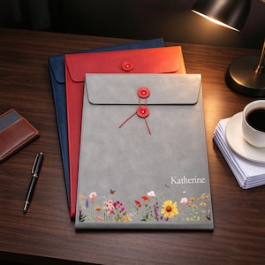 May include: A stack of three document folders in gray, red, and blue. The top gray folder features a string-tie closure, a floral print at the bottom, and the name Katherine printed in white text on the front surface.