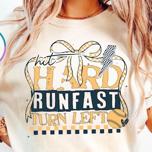 May include: Ivory-colored t-shirt with a baseball-themed graphic. The design features the words "Hit Hard Run Fast Turn Left" in a vintage style, along with a baseball and lightning bolt.