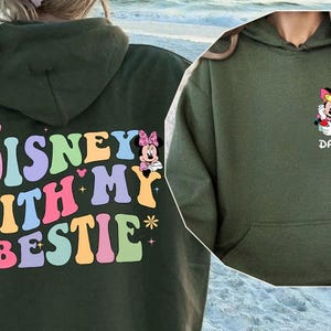 May include: A green hooded sweatshirt with the text "DISNEY WITH MY BESTIE" in colorful letters. The sweatshirt features a cartoon image of Minnie Mouse and Daisy Duck.