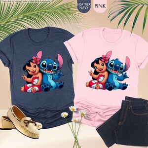 K&ouml;nnte beinhalten: Zwei T-Shirts, eines in Heather Navy und eines in Pink, mit einer Cartoon-Grafik von Lilo und Stitch. Das marinefarbene Shirt wird mit cremefarbenen Loafern kombiniert, und das rosa Shirt wird mit dunkelblauen Jeans kombiniert. Das Bild enth&auml;lt auch den Text "HEATHER NAVY" und "PINK".