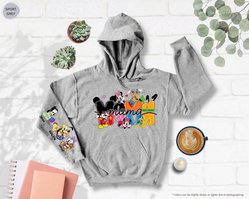 K&ouml;nnte beinhalten: Ein grauer Kapuzenpullover mit dem Wort "Mama" in einem farbenfrohen Disney-Design. Der linke &Auml;rmel zeigt Cartoon-Figuren und Namen. Der Pullover hat eine Kapuze und eine Vordertasche. Er ist aus weichem Material.