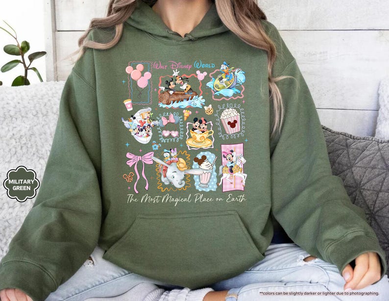 May include: Military green hoodie featuring a colorful graphic of Disney characters and icons. The design includes Mickey and Minnie Mouse, Dumbo, and other elements. Text on the hoodie reads "Walt Disney World" and "The Most Magical Place on Earth."
