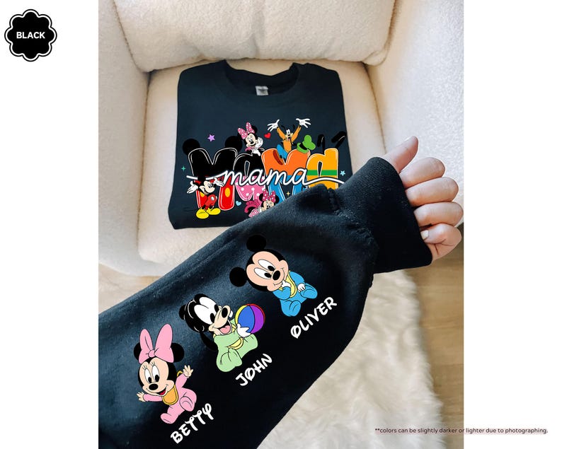 K&ouml;nnte beinhalten: Schwarzes Sweatshirt mit einem farbenfrohen "Mama"-Design mit Mickey- und Minnie-Mouse-Figuren. Der &Auml;rmel zeigt Cartoon-Bilder von Minnie, Mickey und zwei weiteren Figuren mit den Namen "Betty", "John" und "Oliver".